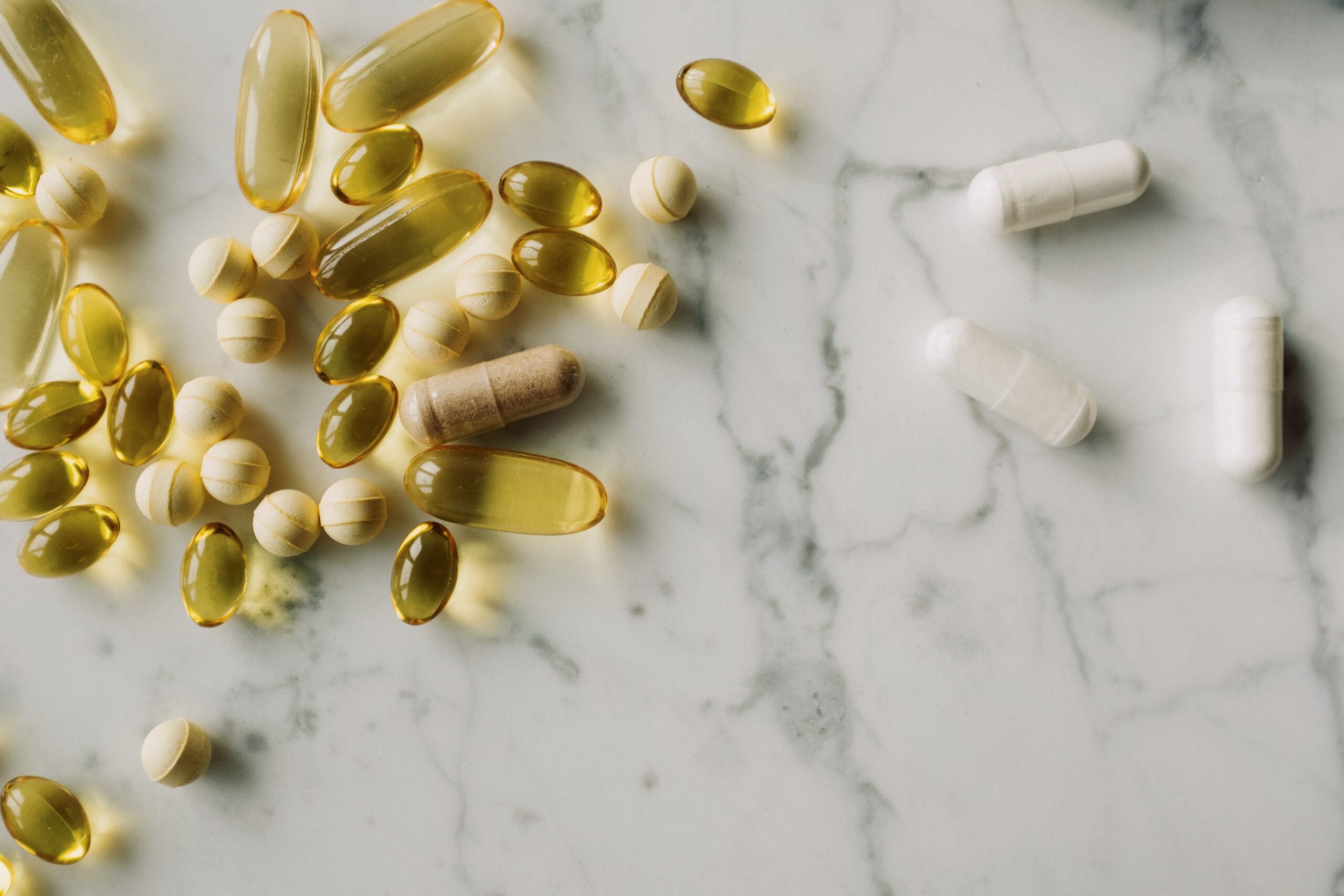 A variety of capsules and pills scattered on a marble surface, offering a modern healthcare concept.