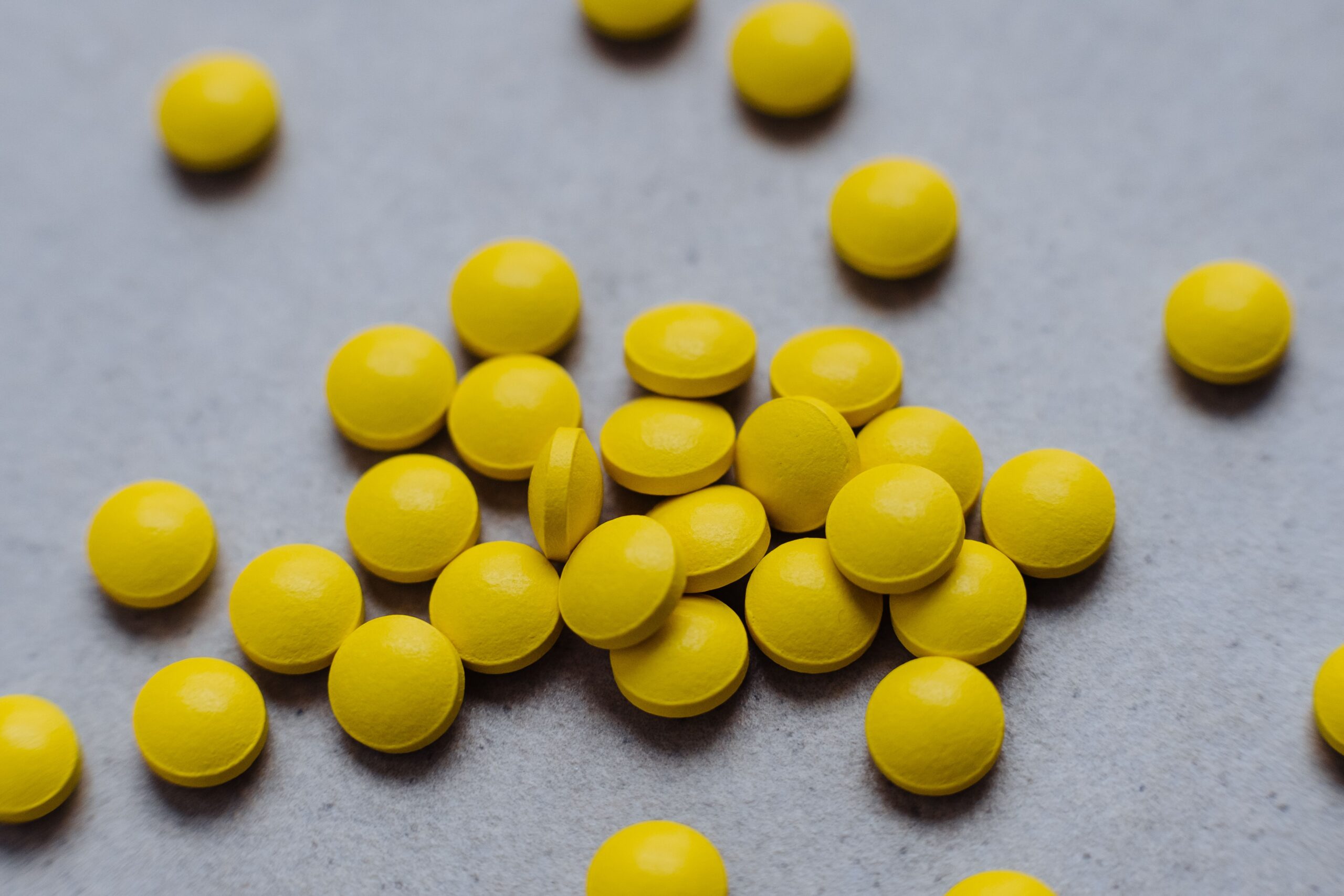 A collection of bright yellow pills scattered on a gray surface, ideal for health and wellness themes.