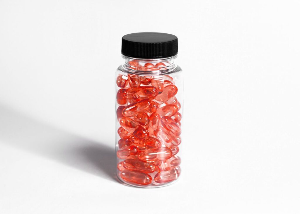 Clear jar filled with red capsules on a white background, perfect for health and wellness themes.